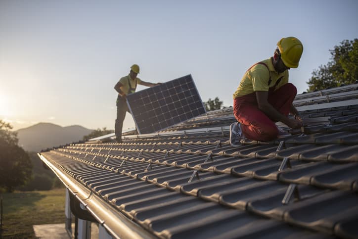 Professional Workers Installing Solar Panels On A Roof At Sunset.