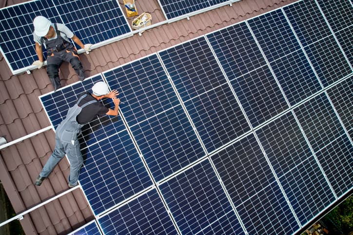 Male technicians install photovoltaic solar panels on top of a roof