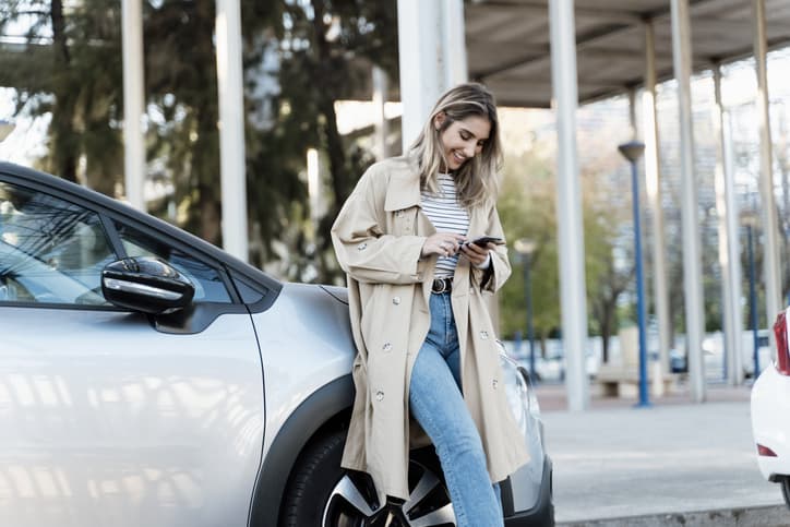 Young woman using smartphone, leaning on her car