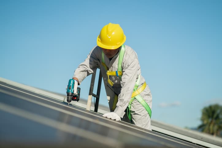 Solar panel technician installing solar panels with a power tool.