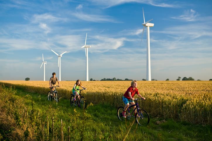 3 children on bicycles in front of wind turbines in a wheat field on a sunny day.