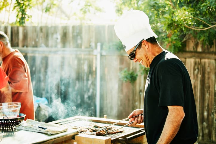 Smiling father wearing a white chef's hat grilling in backyard during family barbecue