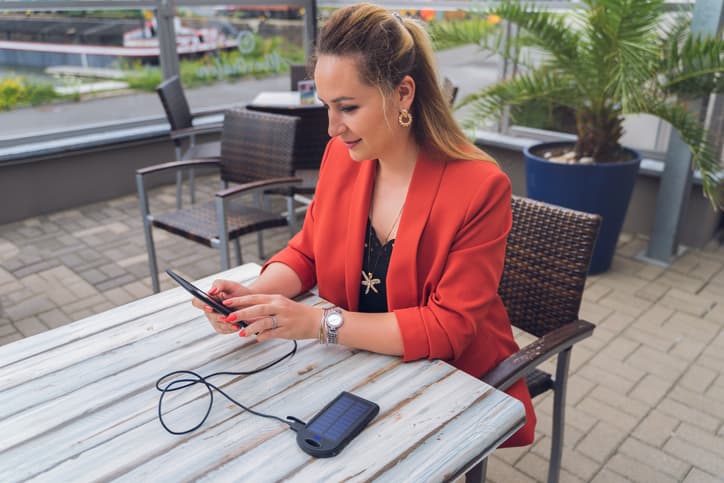 Woman reading her ebook in an outdoor cafe while charging it with a small portable solar panel