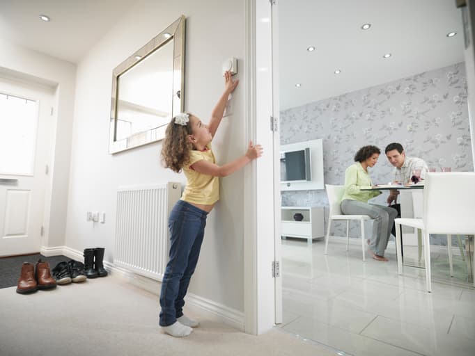 Image of a young girl adjusting the thermostat in energy efficient house as parents sit in the living room